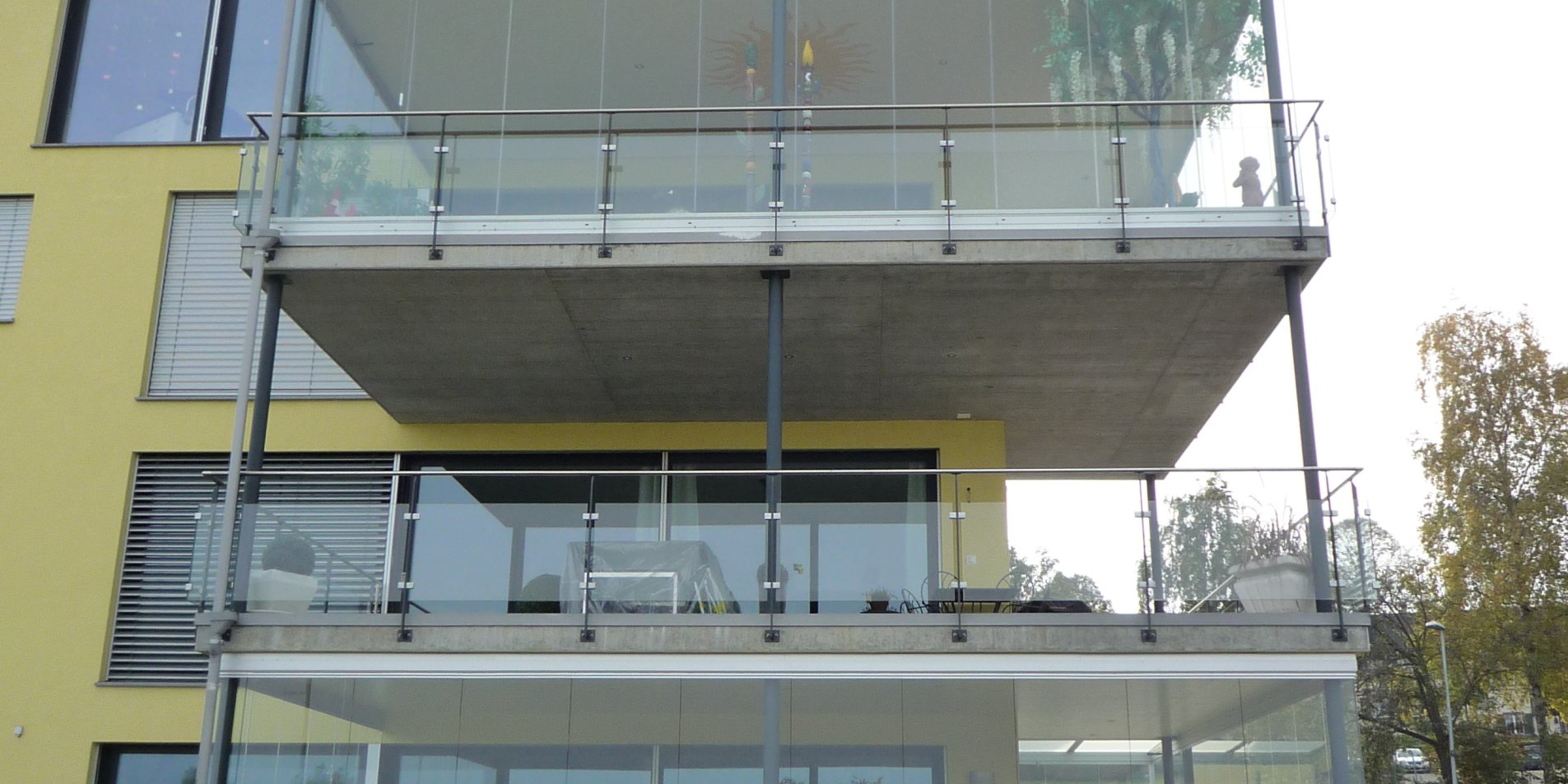 Mehrgeschossiger Balkonturm mit COVER Schiebe-Drehverglasung an einem gelben Wohnhaus