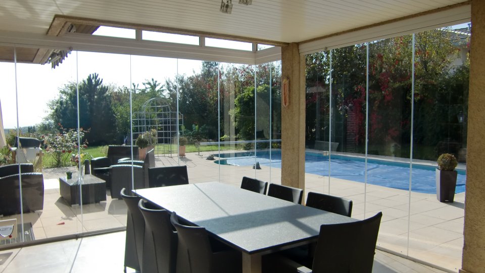 Sitzplatz mit COVER Schiebe-Drehverglasung, grossem Esstisch und Blick auf den Pool